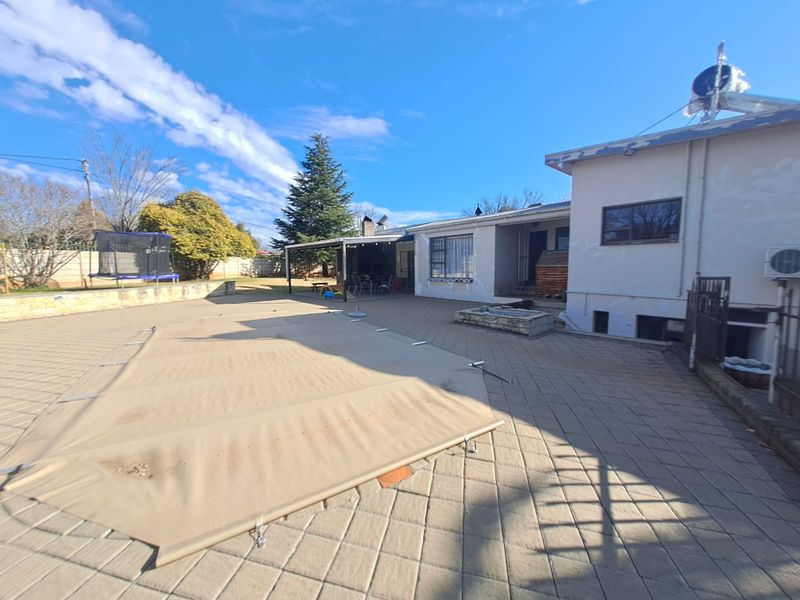 Rear exterior view featuring a paved patio area, a covered outdoor space, and a swimming pool with a safety cover.