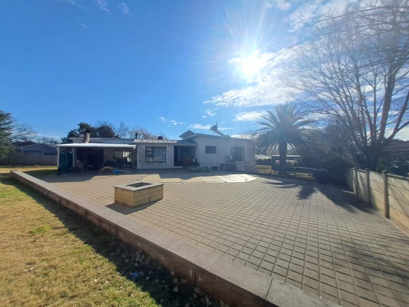 Spacious rear exterior featuring a large paved patio area, a covered entertainment space, and a built-in fire pit in the garden.