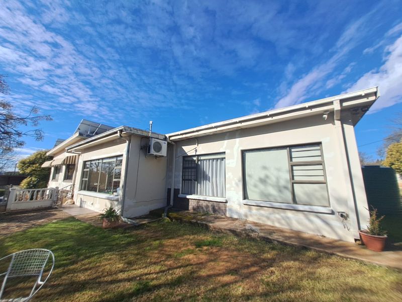 Rear elevation of the house featuring solar panels, an external air conditioning unit, and aluminium window frames, showing signs of weathered exterior paint and plaster.