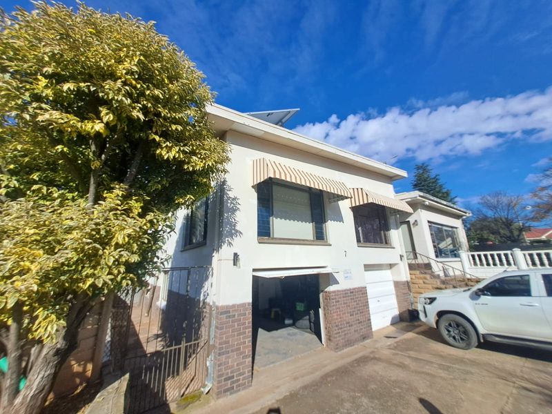 Front elevation of a multi-level house featuring a garage, brick base detailing, and window awnings under a clear blue sky.
