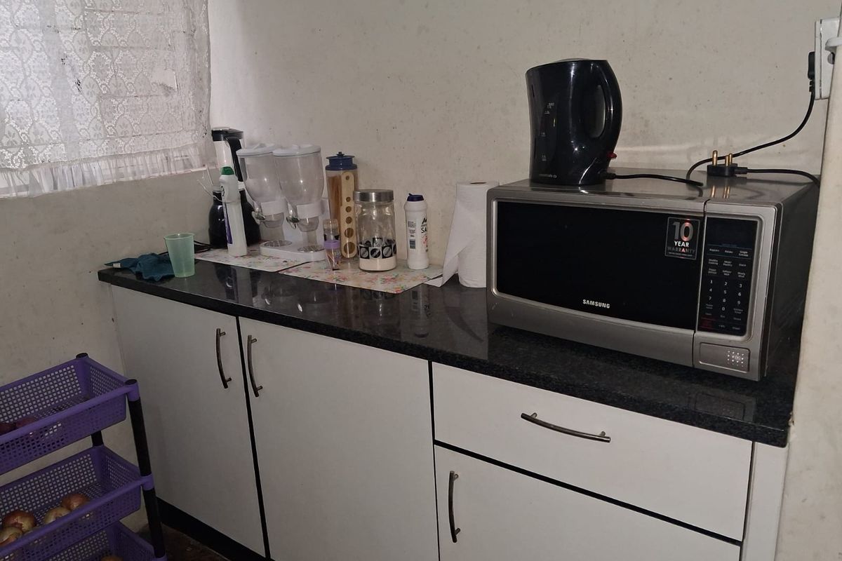 A compact kitchen area featuring white cabinetry, dark granite countertops, and a built-in microwave space.