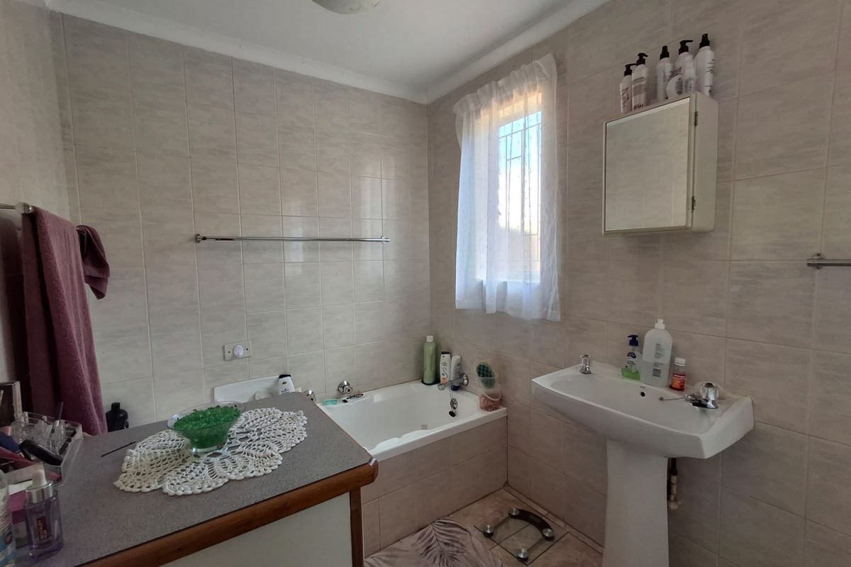 A functional bathroom featuring a built-in bathtub, pedestal washbasin, and wall-mounted medicine cabinet with neutral ceramic wall tiling.