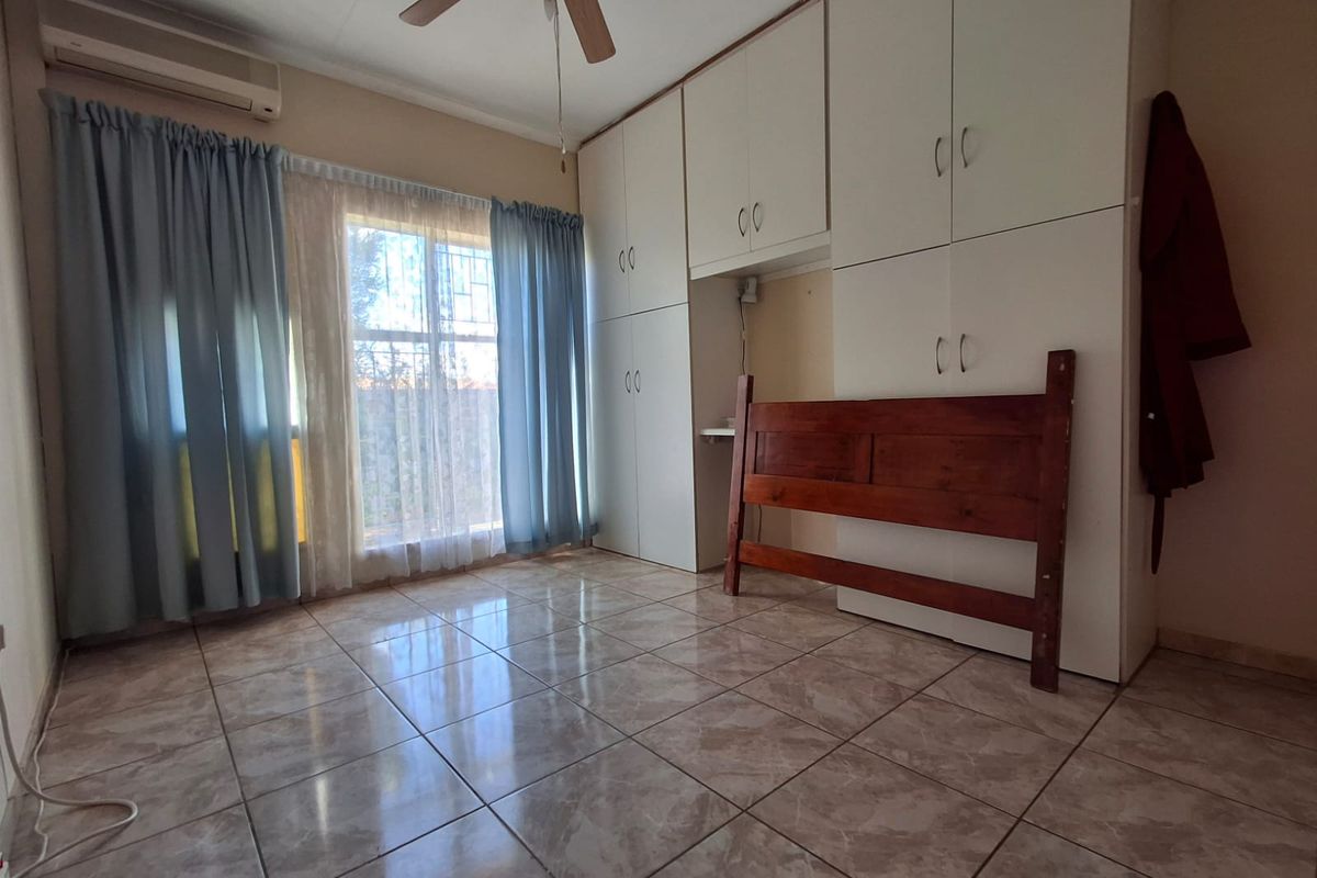 A bedroom featuring built-in cupboards, tiled flooring, a ceiling fan, and an air conditioning unit.