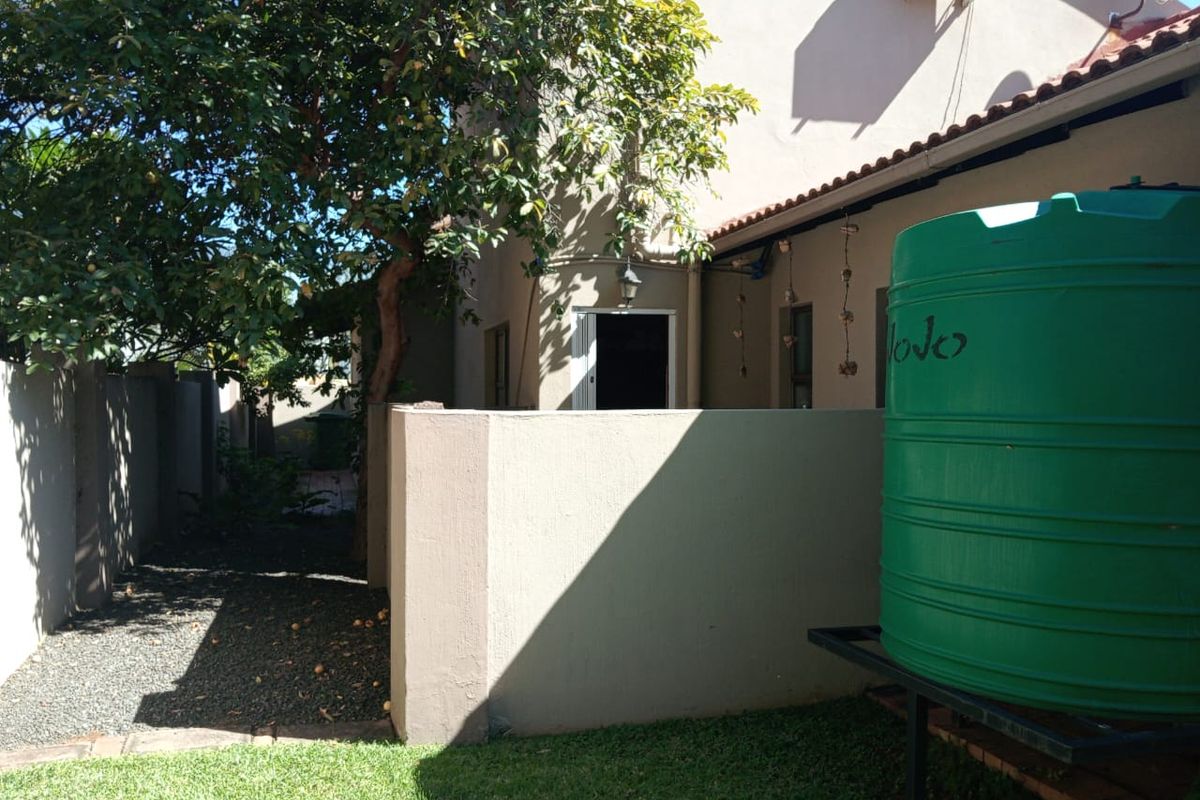 Rear exterior view of the townhouse featuring a green water storage tank, boundary wall, and established garden area with gravel pathway.