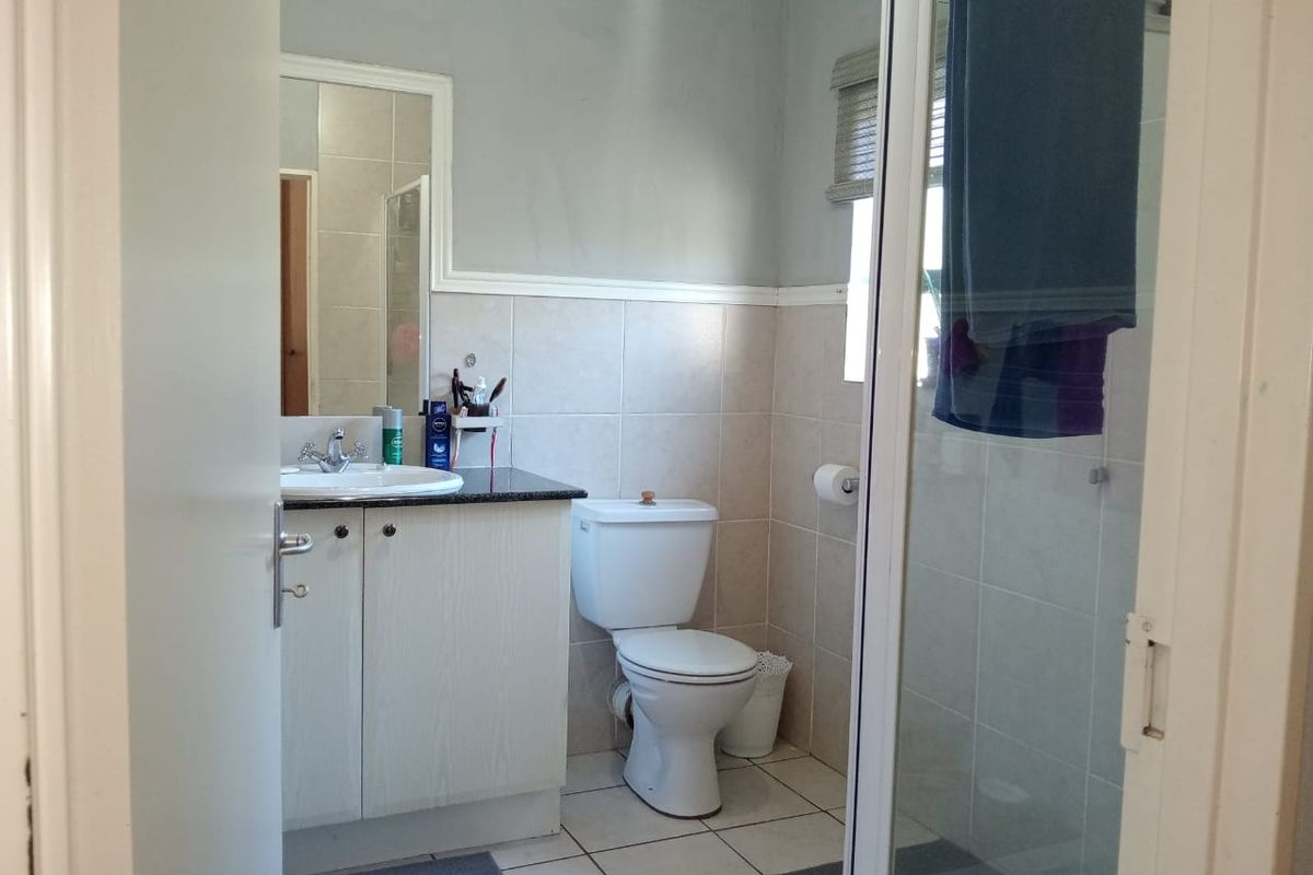 A functional bathroom featuring a vanity cabinet with granite countertop, a toilet, and a glass-enclosed shower with neutral wall and floor tiling.
