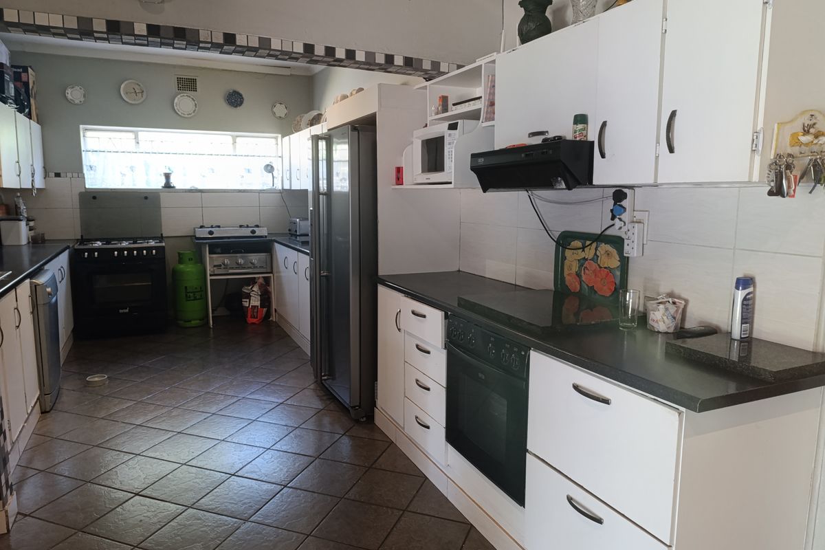 A functional kitchen featuring white cabinetry, dark countertops, tiled flooring, and integrated appliances including an oven and extractor fan.