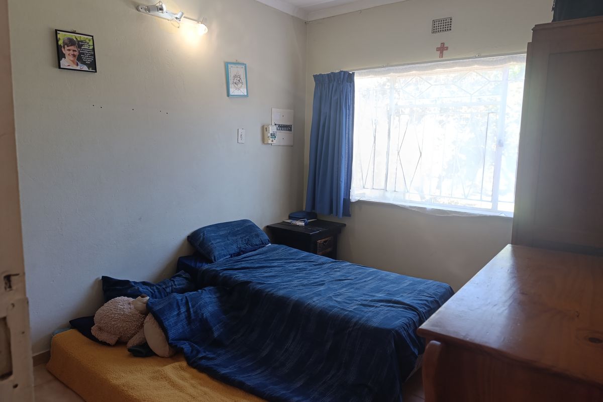 A bedroom featuring a window with security bars, wall-mounted lighting, and an electrical distribution board, requiring cosmetic updates to improve its overall condition.