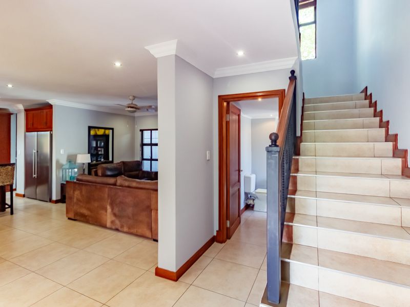 Open plan living area featuring tiled flooring, a staircase with a wooden handrail, and a modern kitchen with integrated appliances.