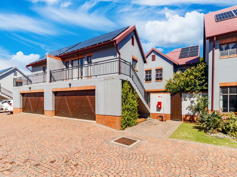 Front view of a modern townhouse complex featuring a brick-paved driveway, double garages, solar panels, and an external staircase leading to an upper balcony.