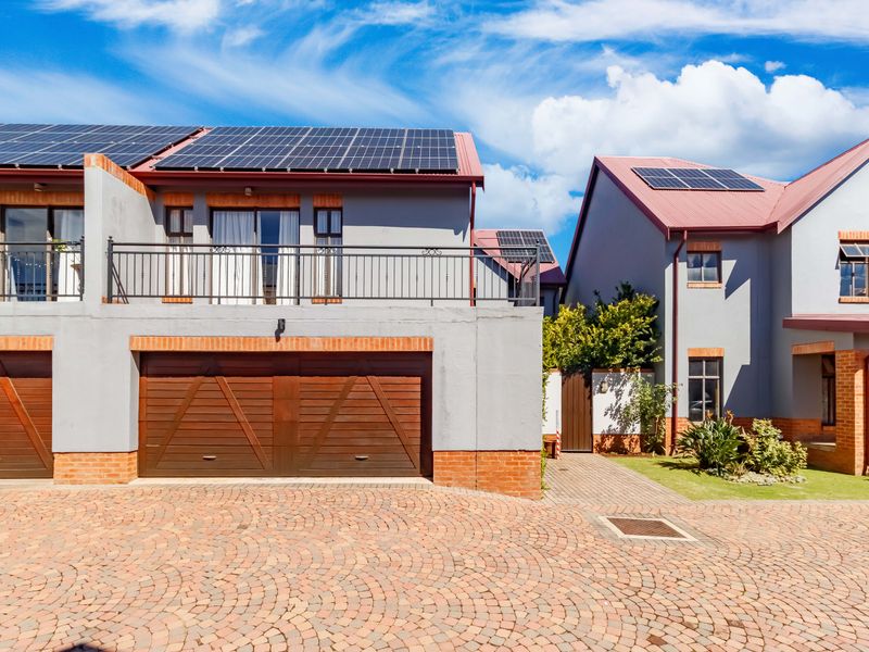 Front view of a modern townhouse complex featuring solar panels, a double garage, and a balcony with metal railings.