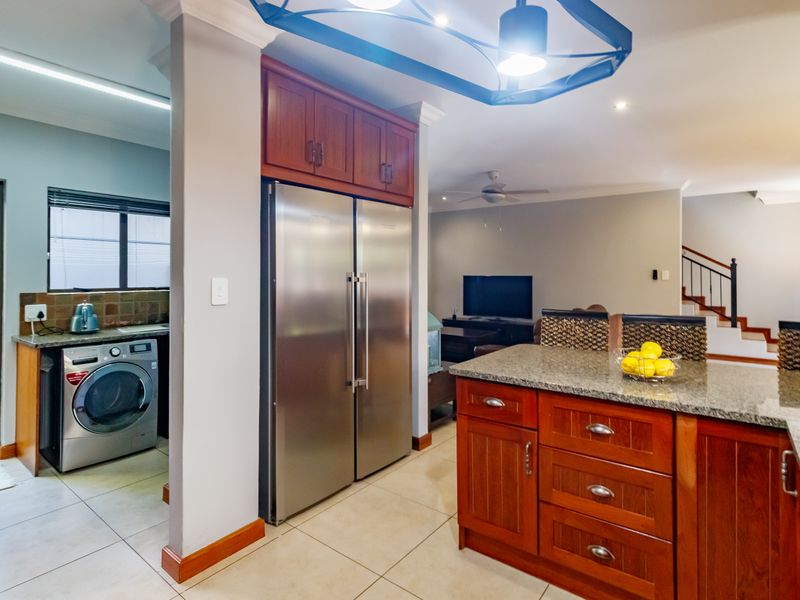 Open plan kitchen and living area featuring granite countertops, wooden cabinetry, tiled flooring, and a staircase leading to the upper level.