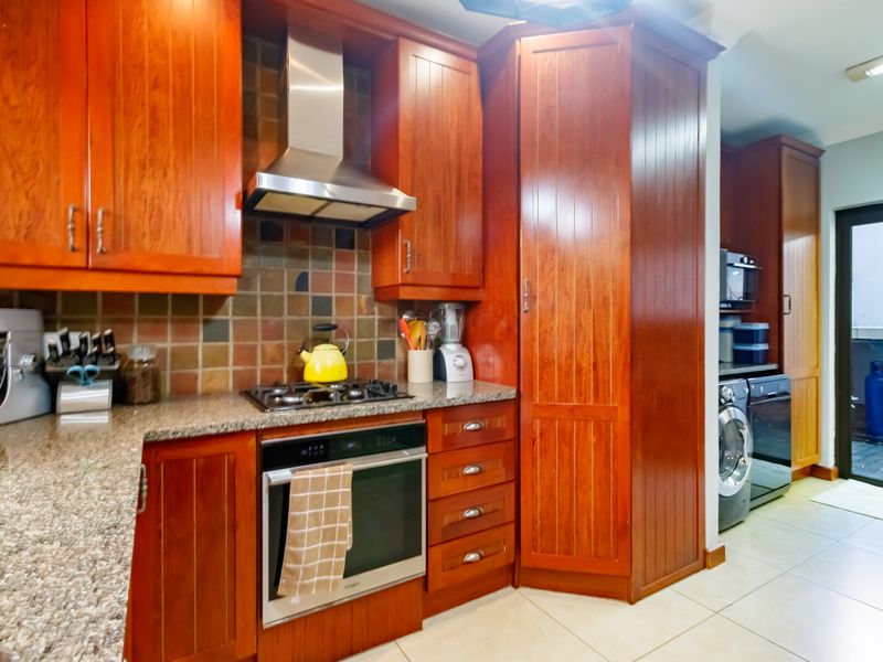 A functional kitchen featuring warm-toned wooden cabinetry, granite countertops, a gas hob, and an integrated laundry area with direct access to an outdoor space.