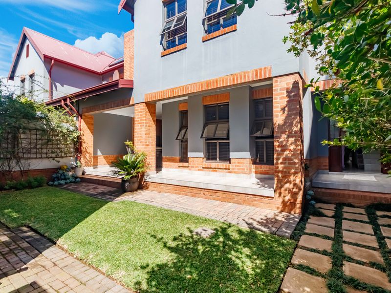 Rear view of the townhouse featuring a covered patio, brick detailing, paved pathways, and a well-maintained garden area.
