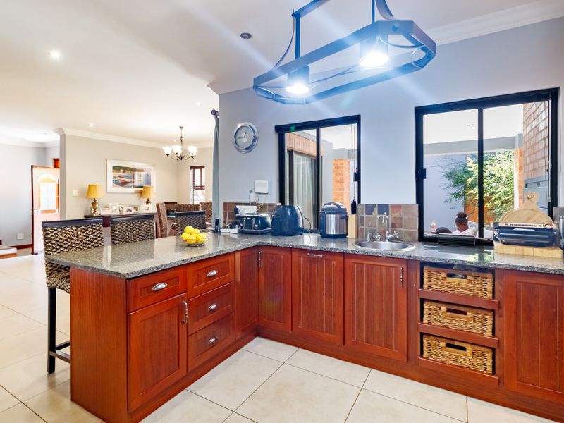 Open plan kitchen featuring warm wooden cabinetry, granite countertops, and tiled flooring, seamlessly flowing into the adjacent living and dining areas.