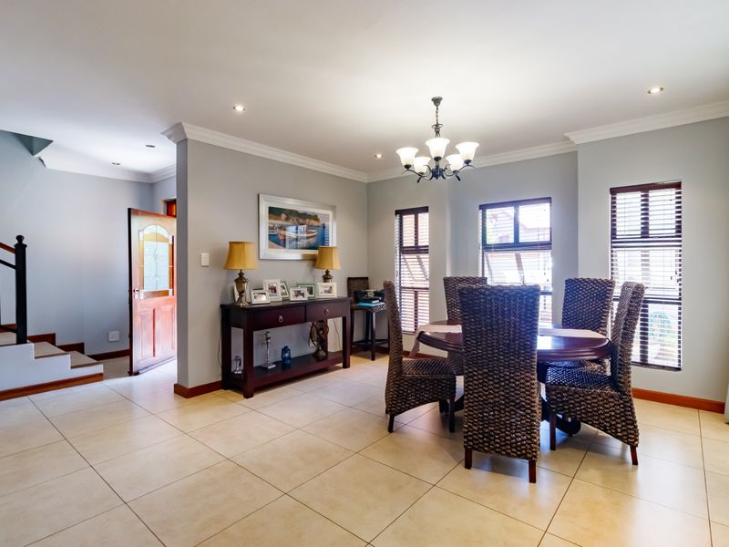A bright dining area featuring tiled flooring, a classic chandelier, and a timber staircase leading to the upper level.