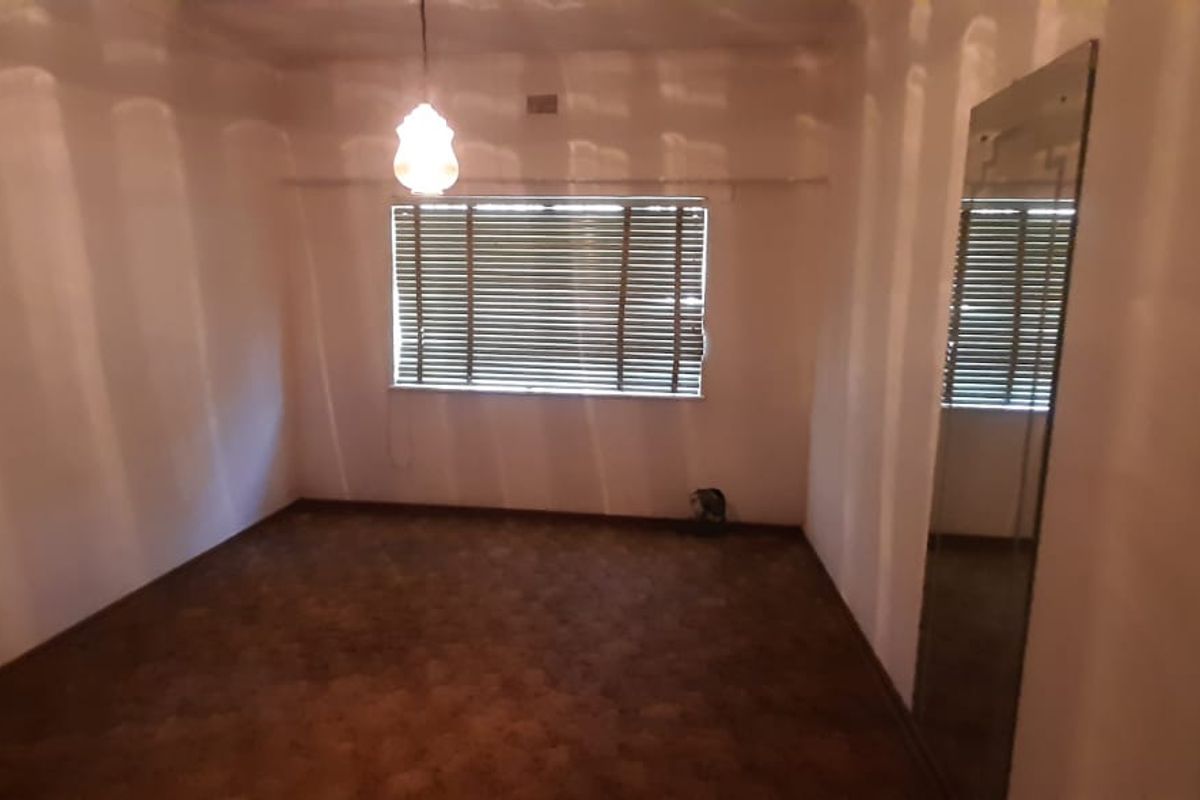 A vacant bedroom featuring carpeted flooring, a window with horizontal blinds, and a built-in mirror.