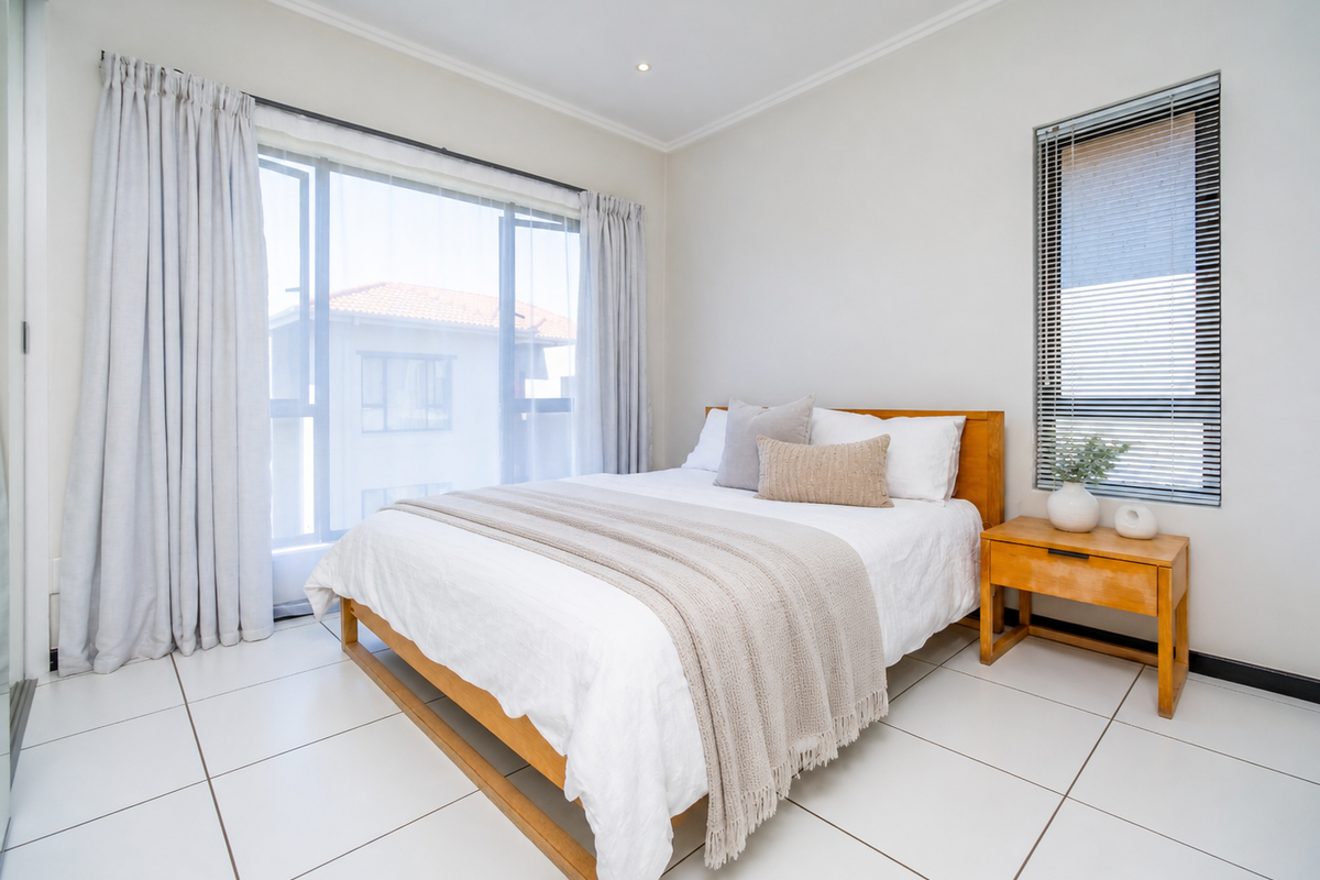 A bright and modern bedroom featuring large sliding glass doors, neutral tiled flooring, and clean white walls, offering a comfortable and well-lit living space.