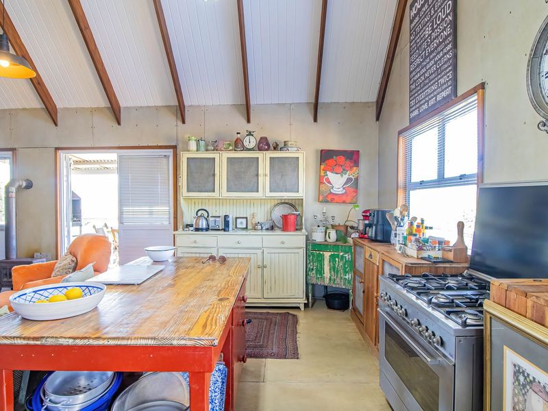 Rustic kitchen featuring vaulted ceilings with exposed timber beams, a gas stove, and direct access to an outdoor area through sliding glass doors.