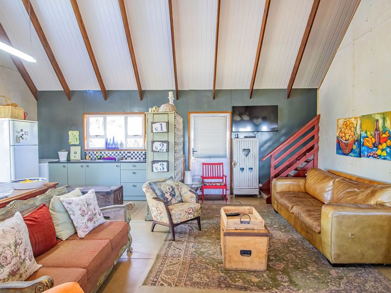 Open-plan living area featuring a vaulted ceiling with exposed timber beams, integrated kitchen cabinetry, and a timber staircase leading to an upper level.