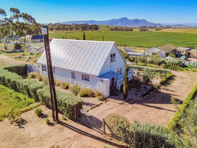 Aerial view of a rural property featuring a white house with a corrugated metal roof, surrounding garden, and expansive countryside views.