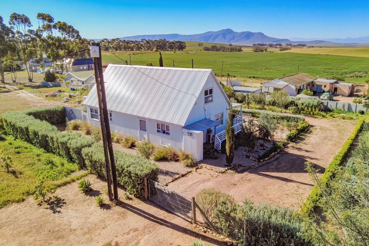 Aerial view of a rural property featuring a white house with a corrugated metal roof, surrounding garden, and expansive countryside views.