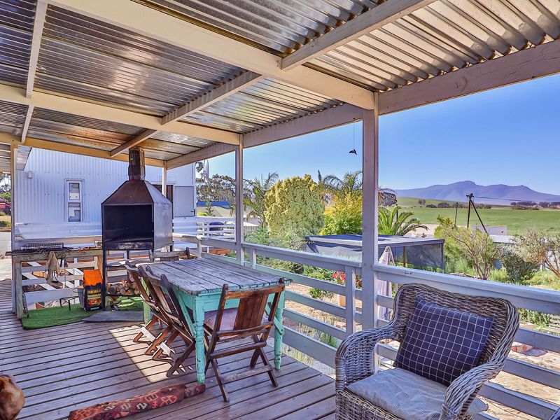 Covered outdoor patio featuring timber decking, a built-in braai, and scenic rural views, providing an ideal space for outdoor entertaining.