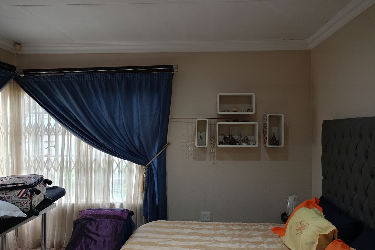 A bedroom featuring a window with a security gate, curtain rails, and decorative wall-mounted shelving units.