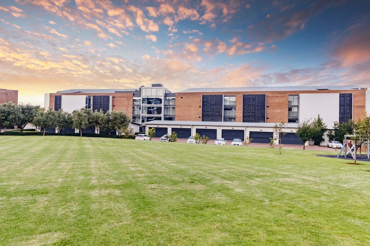 A wide-angle view of the apartment complex exterior, featuring a large manicured lawn, integrated garage units, and modern brick and render facade architecture.