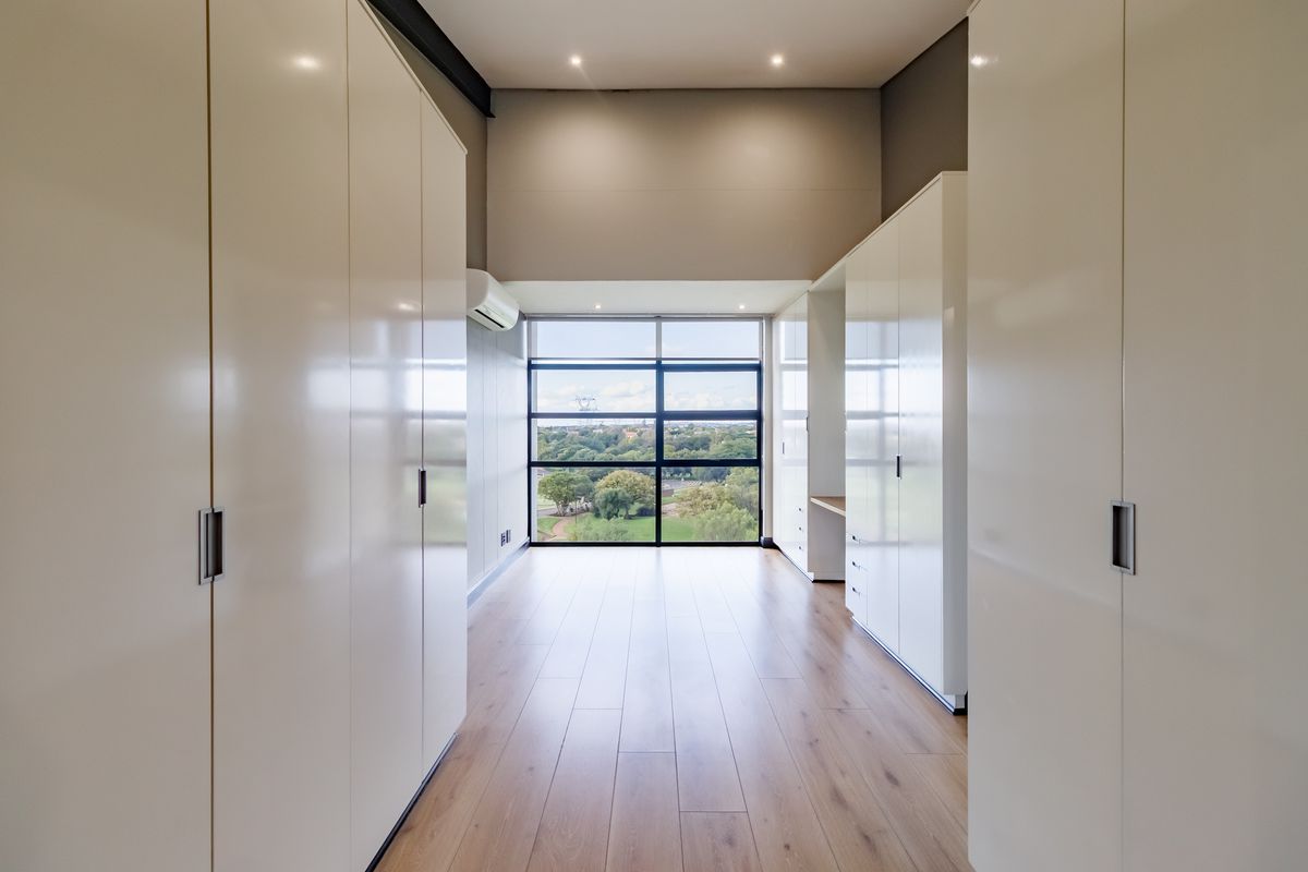 A bright, modern bedroom featuring extensive built-in cabinetry, light wood-look flooring, and a large window offering expansive green views.