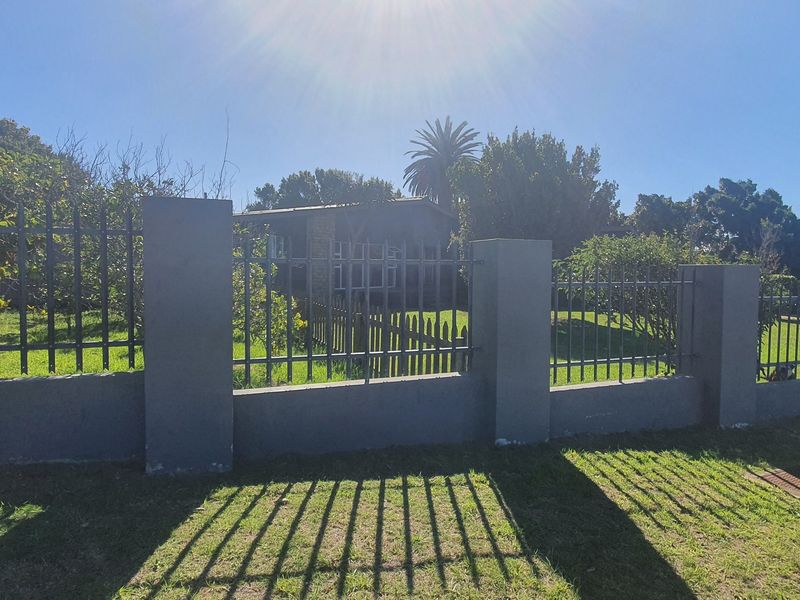 A view of the property's front boundary featuring a secure metal fence with concrete pillars and a well-maintained lawn.