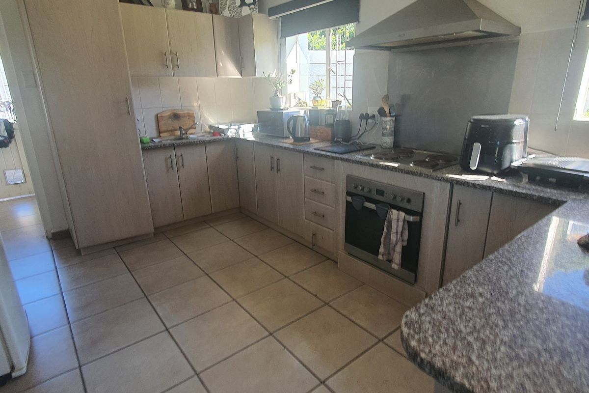 A functional kitchen featuring light wood-finish cabinetry, granite countertops, built-in oven, and hob with a tiled splashback and floor.