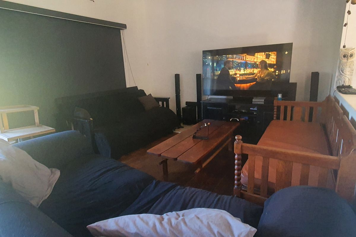 A living room featuring hardwood flooring and a sliding glass door with a roller blind, providing access to the outdoor area.