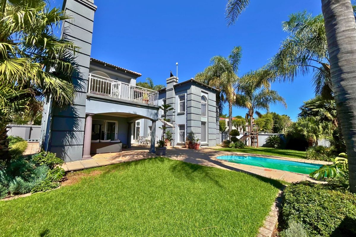 Rear view of a multi-story residence featuring a covered patio, balcony, swimming pool, and landscaped garden area.