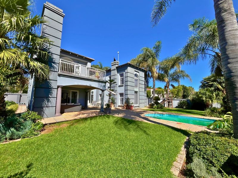 Rear view of a multi-story residence featuring a covered patio, balcony, swimming pool, and landscaped garden area.