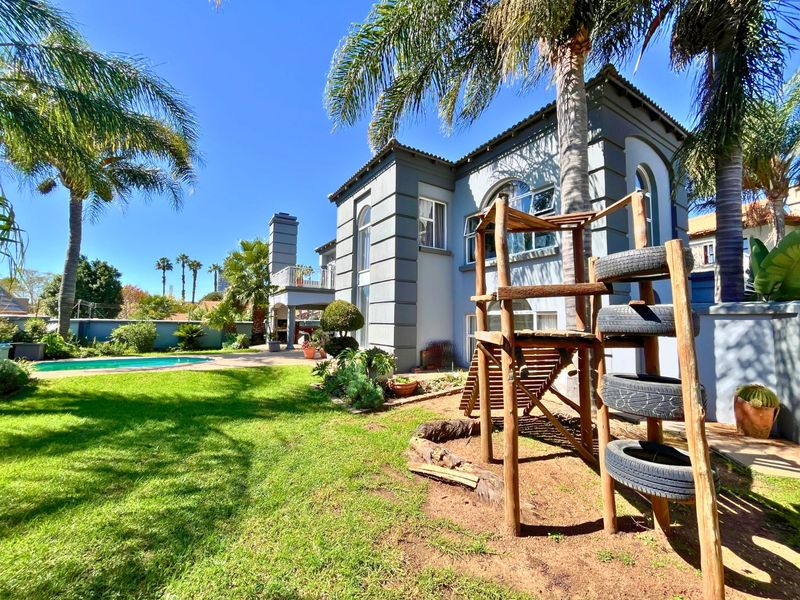 Rear view of the property featuring a landscaped garden, swimming pool, and a covered patio area with an outdoor fireplace.