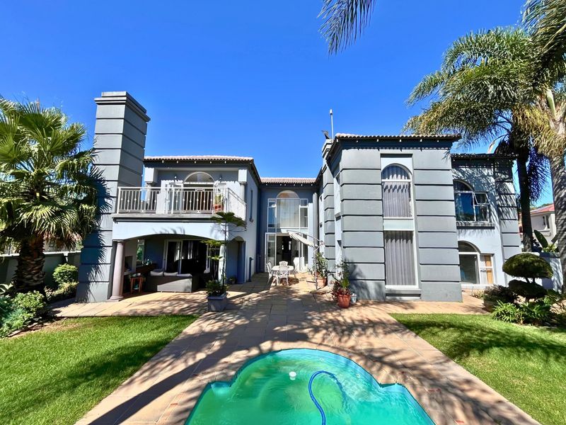 Rear view of a multi-story residence featuring a paved patio, swimming pool, balcony, and established garden landscaping.