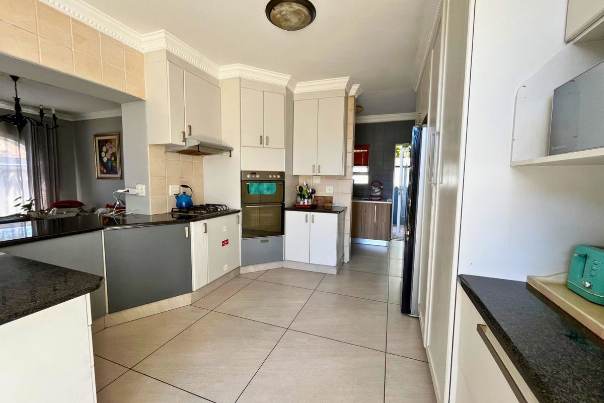 Functional kitchen featuring built-in oven, hob, extractor fan, and granite countertops with ample cabinetry and tiled flooring.