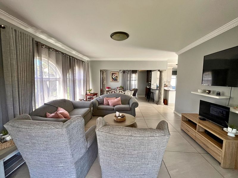 Spacious open-plan living area featuring tiled flooring, decorative crown molding, and architectural columns connecting to the dining and kitchen spaces.