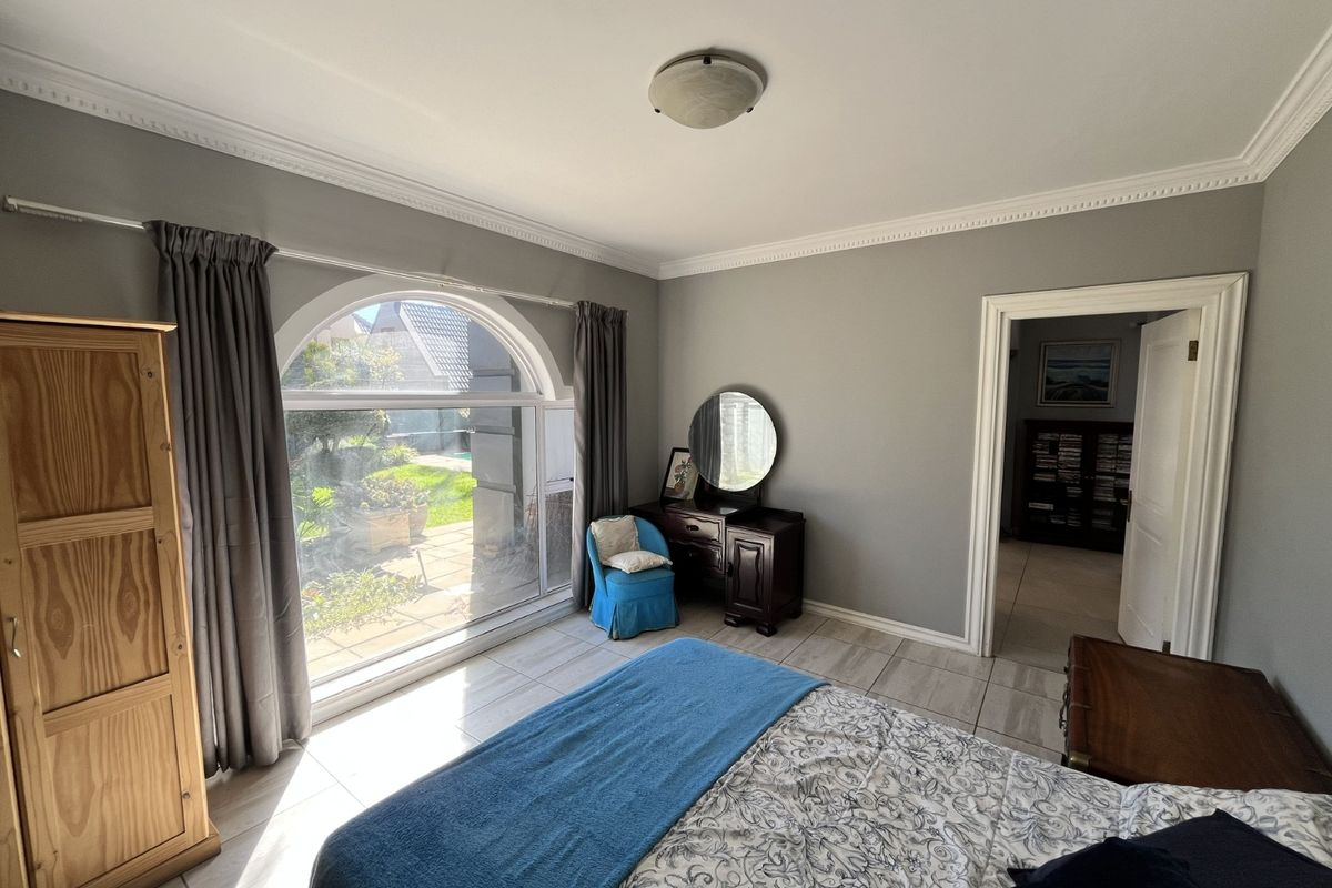 A bright bedroom featuring large arched windows, tiled flooring, and decorative crown molding, offering a view of the garden.