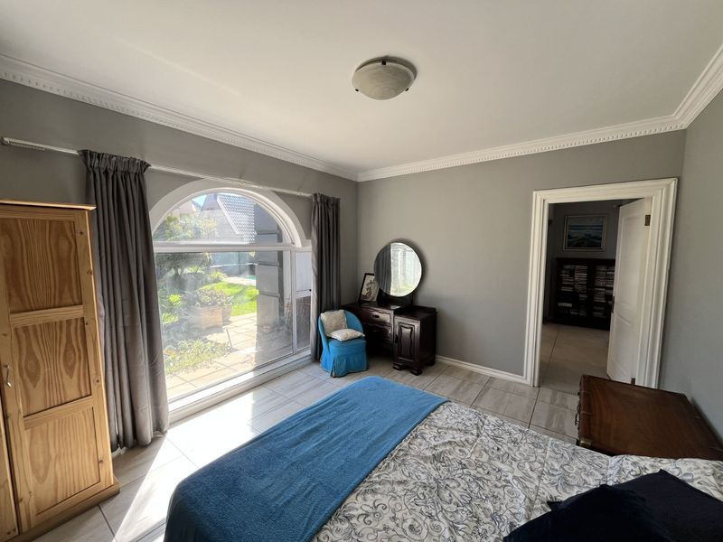 A bright bedroom featuring large arched windows, tiled flooring, and decorative crown molding, offering a view of the garden.