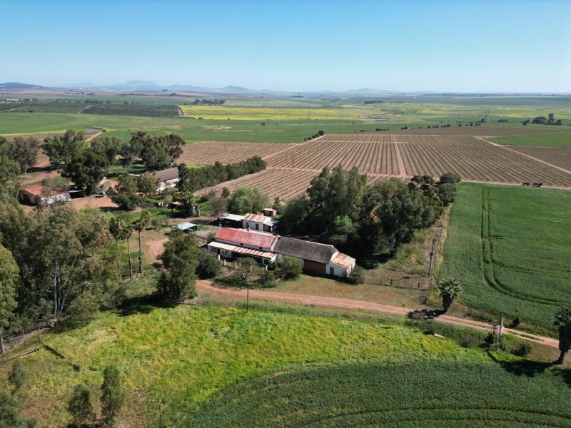 Aerial view of a rural farm property featuring multiple outbuildings, corrugated metal roofing, and extensive surrounding agricultural land.