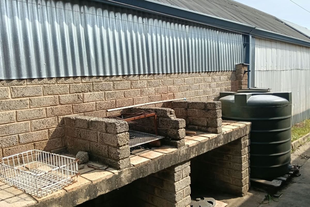 Outdoor area featuring a built-in brick braai station and a large water storage tank against a corrugated metal wall.