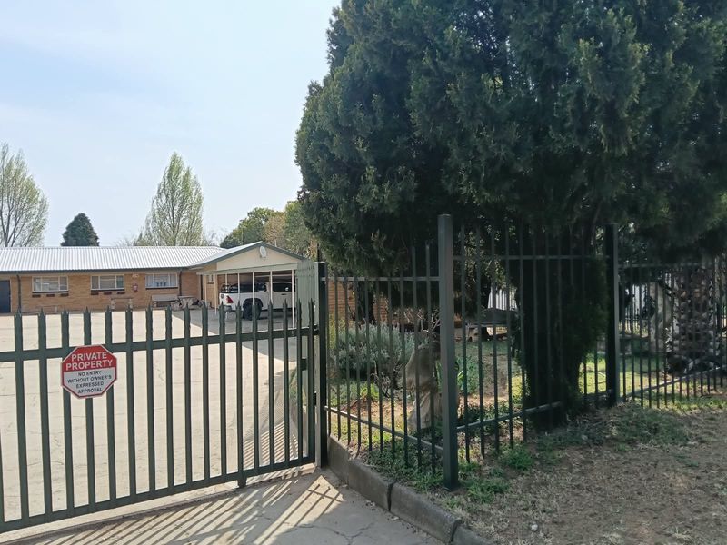 Front view of the property featuring a paved driveway, carport, and secure metal perimeter fencing with a gated entrance.