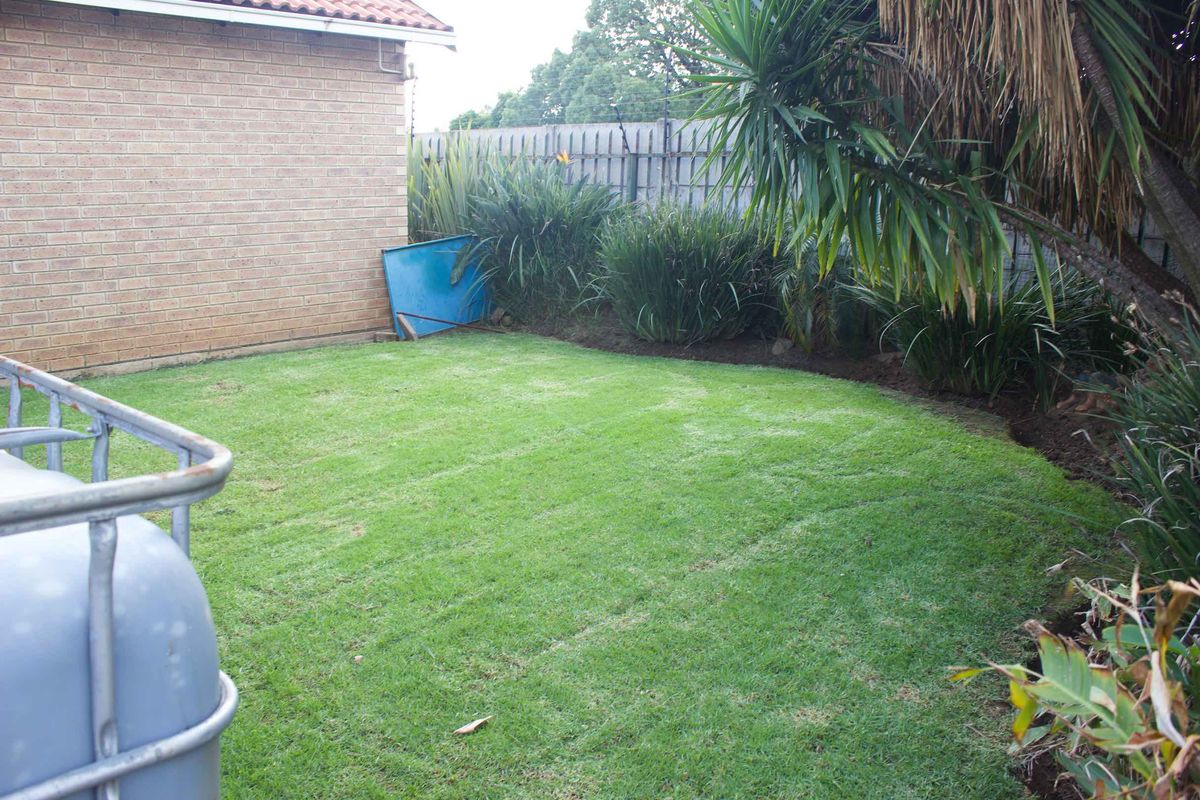 A private rear garden area featuring a well-maintained lawn, brick exterior wall, and perimeter fencing.