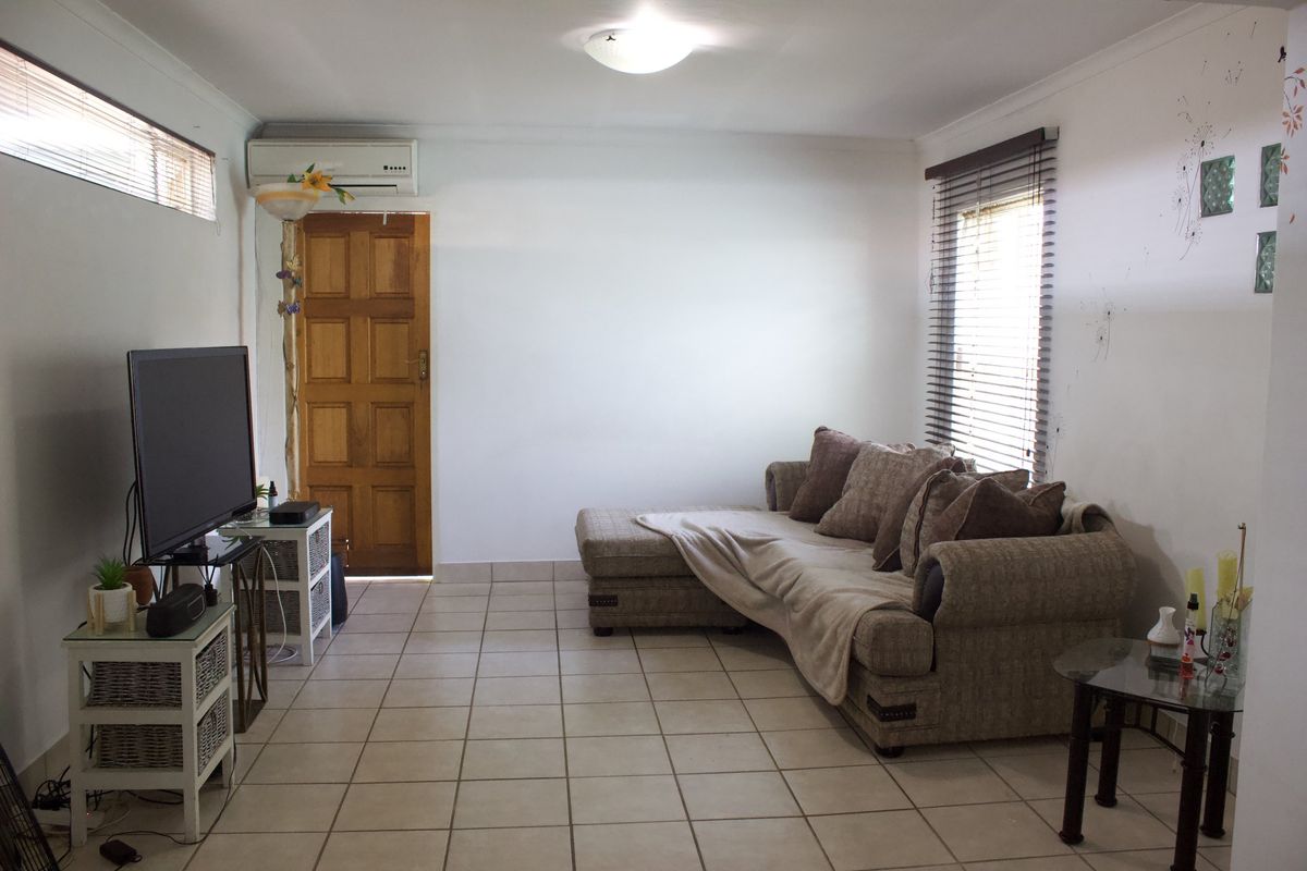 A functional living room featuring tiled flooring, a split-system air conditioner, and natural light through venetian blinds.