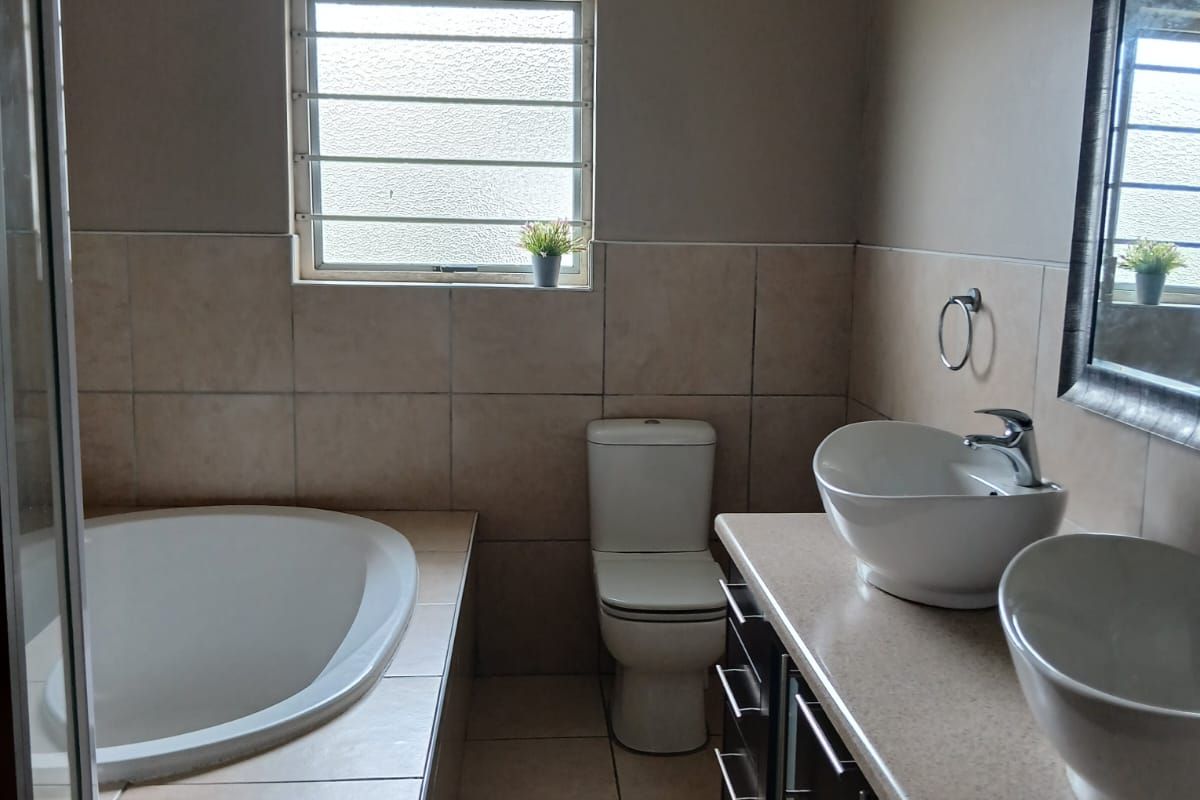A functional bathroom featuring a built-in bathtub, dual vessel sinks on a vanity cabinet, a toilet, and a separate shower enclosure with tiled finishes.