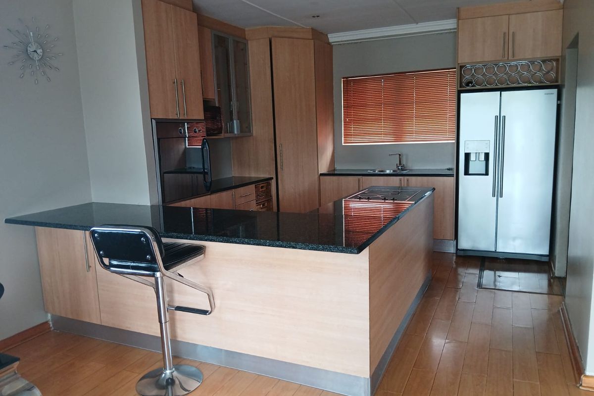 A functional kitchen featuring light wood cabinetry, dark granite countertops, a breakfast bar, and integrated appliances, set against a neutral backdrop with laminate flooring.