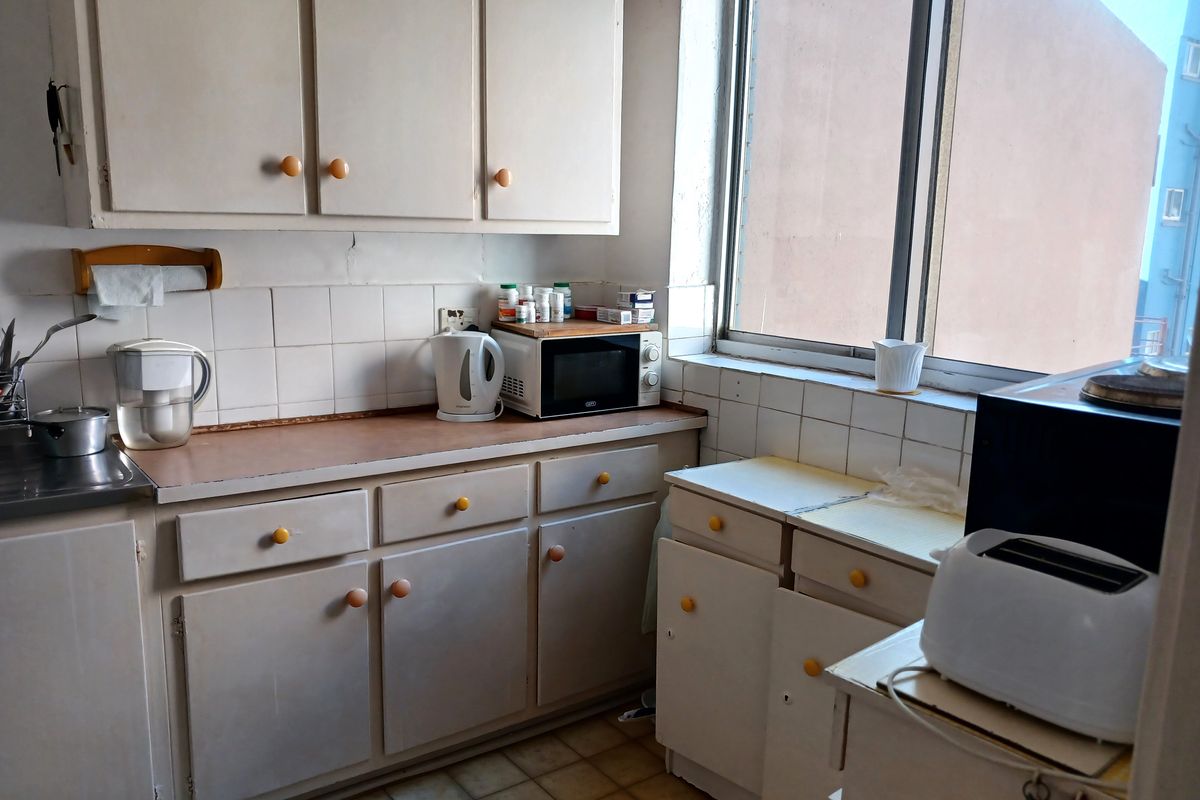 A dated kitchen featuring original cabinetry, tiled backsplash, and a window providing natural light. The space offers a functional layout for renovation.