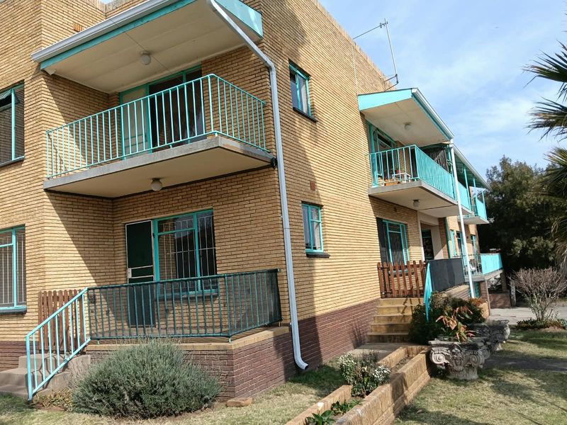 Exterior view of a multi-story apartment building featuring yellow brick facade, private balconies with metal railings, and ground-level access stairs.