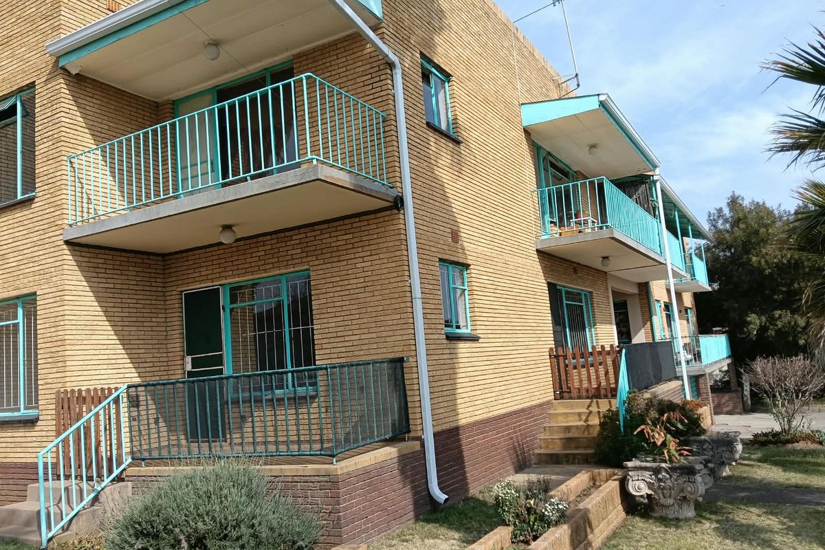 Exterior view of a multi-story apartment building featuring yellow brick facade, private balconies with metal railings, and ground-level access stairs.
